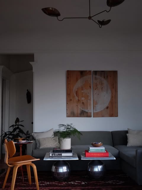 A living room at dusk with a grey sectional, brass pendant, patterned rug and a large diptych artwork on reclaimed wood.